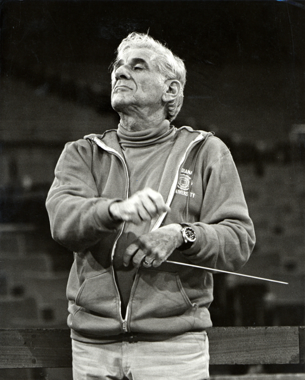 Leonard Bernstein from the waist up, wearing a turtleneck and a crimson IU sweatshirt and holding a conductor's baton.