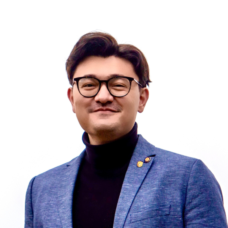 Man wearing glasses, a black turtleneck, and a blue blazer in front of a white background.