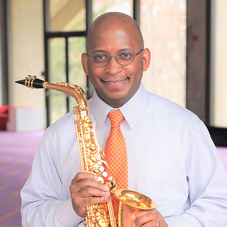 Man holding a saxophone, standing in the MAC lobby.