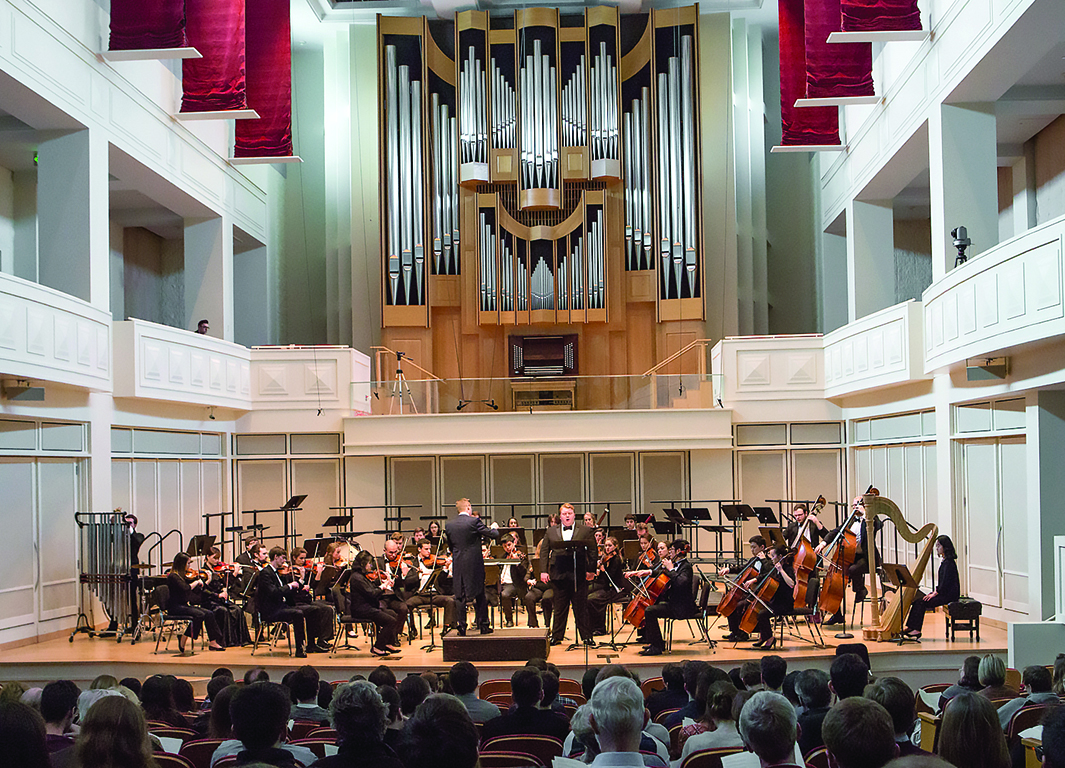 NOTUS performance in Auer hall. Audience members sit and watch an orchestra perform, with a vocal soloist standing center stage.