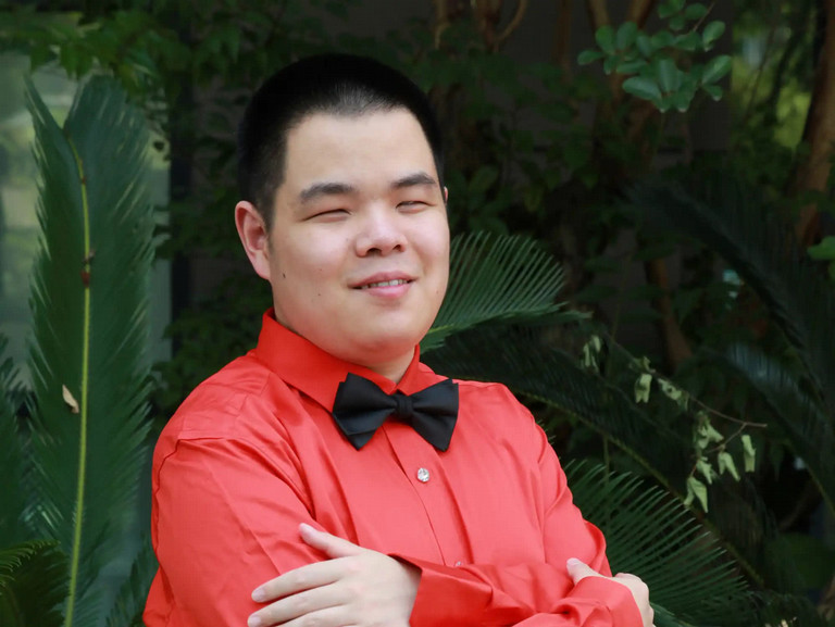 Hans-Derek Yu, sitting at a piano smiling and wearing a tuxedo